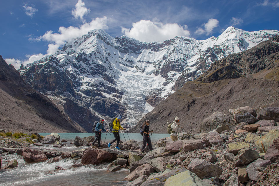 El lago Upis Cocha de color turquesa y los picos nevados. Lago de montaña Ausangate con aguas turquesas frente a picos nevados y rocas en la orilla TreXperience