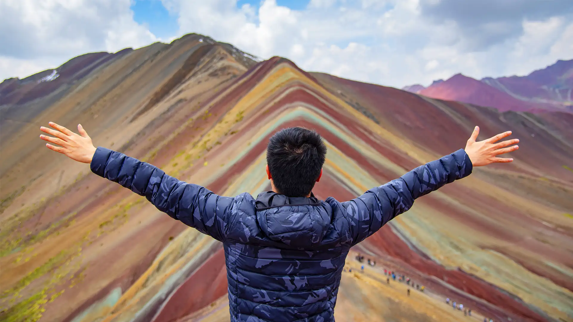 Viajero con los brazos abiertos en frente de la montaña de colores Vinicunca