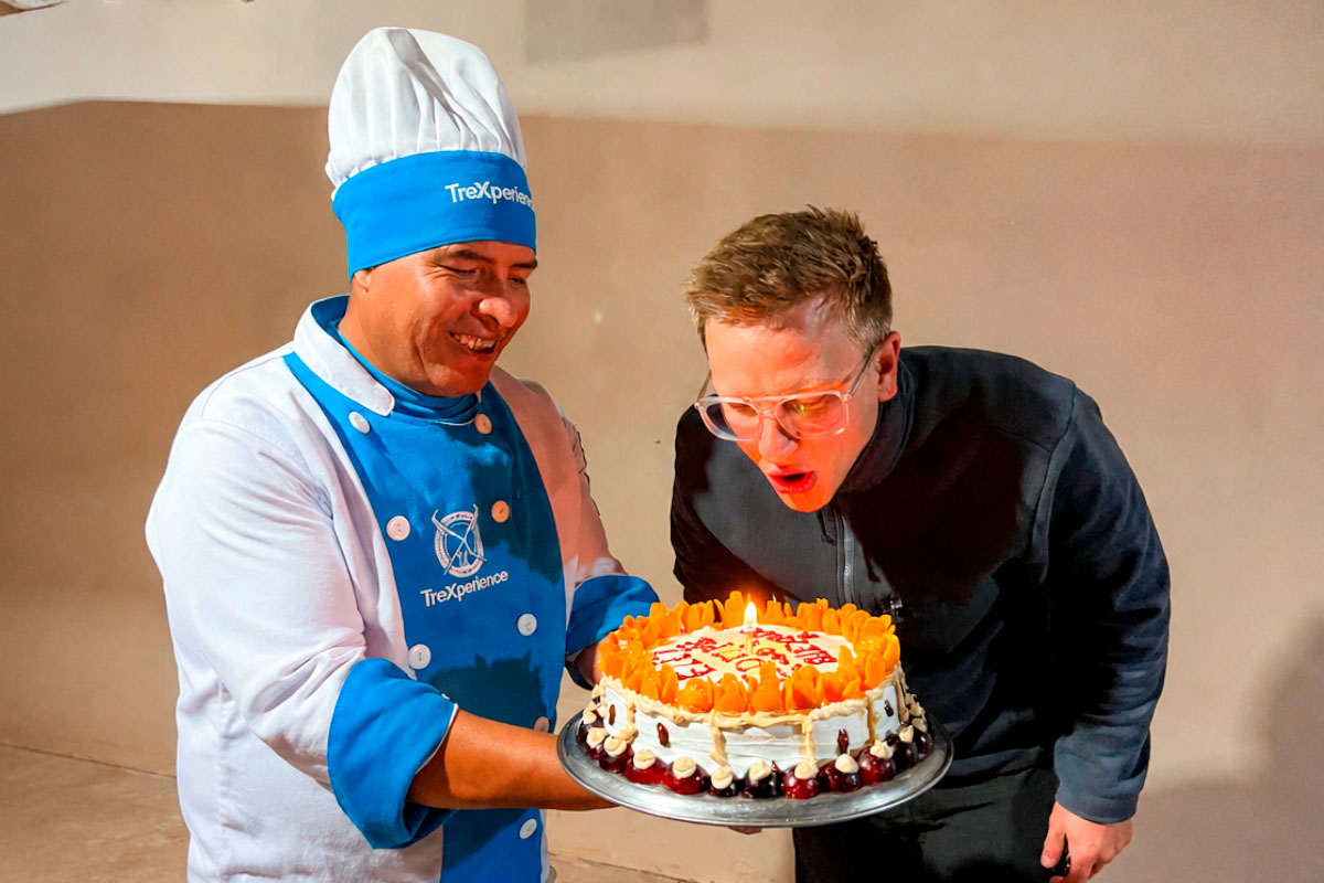 Chef con uniforme azul sosteniendo un pastel de cumpleaños decorado junto a turista | TreXperience