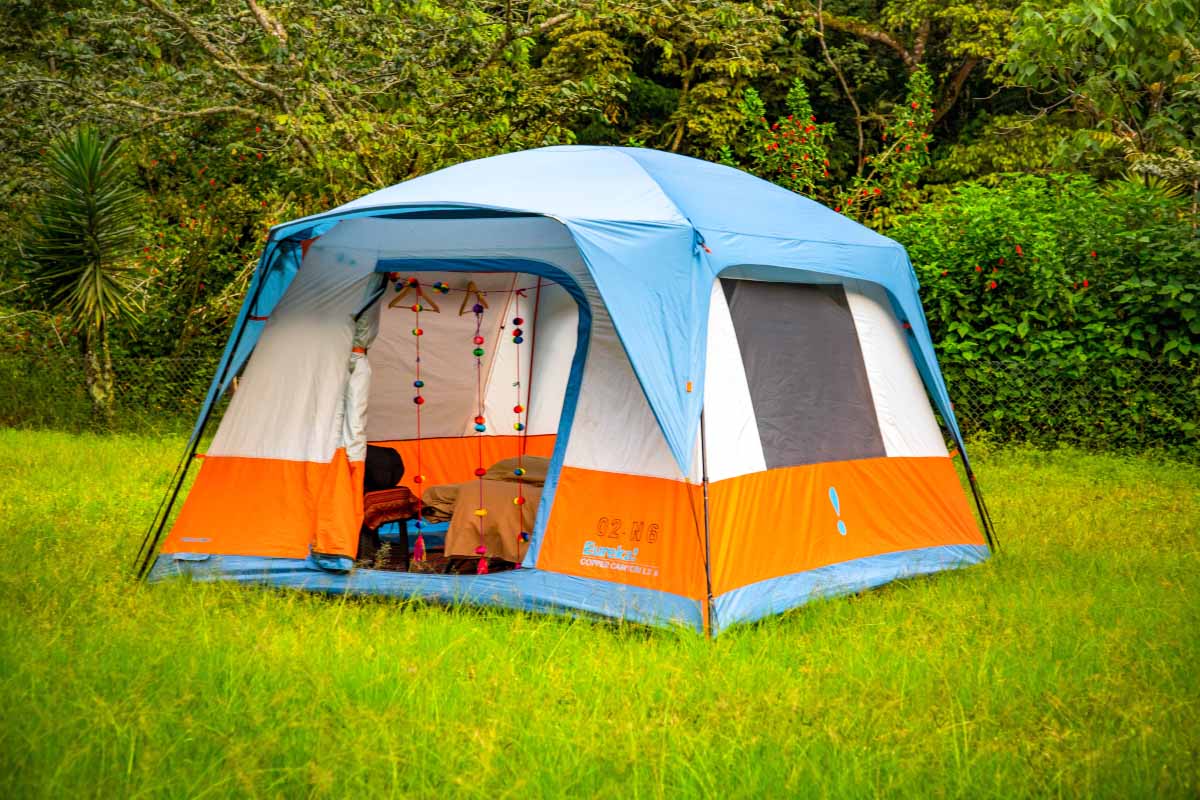 Luxury tent Blue and orange tent set up on green grass, with the entrance open and vegetation in the background | TreXperience