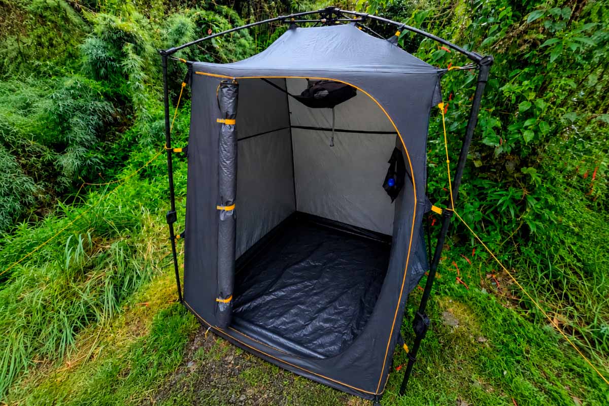 Portable shower cabin on a vegetated hillside Grey shower cubicle installed on grassy terrain, surrounded by green vegetation on a hillside | TreXperience