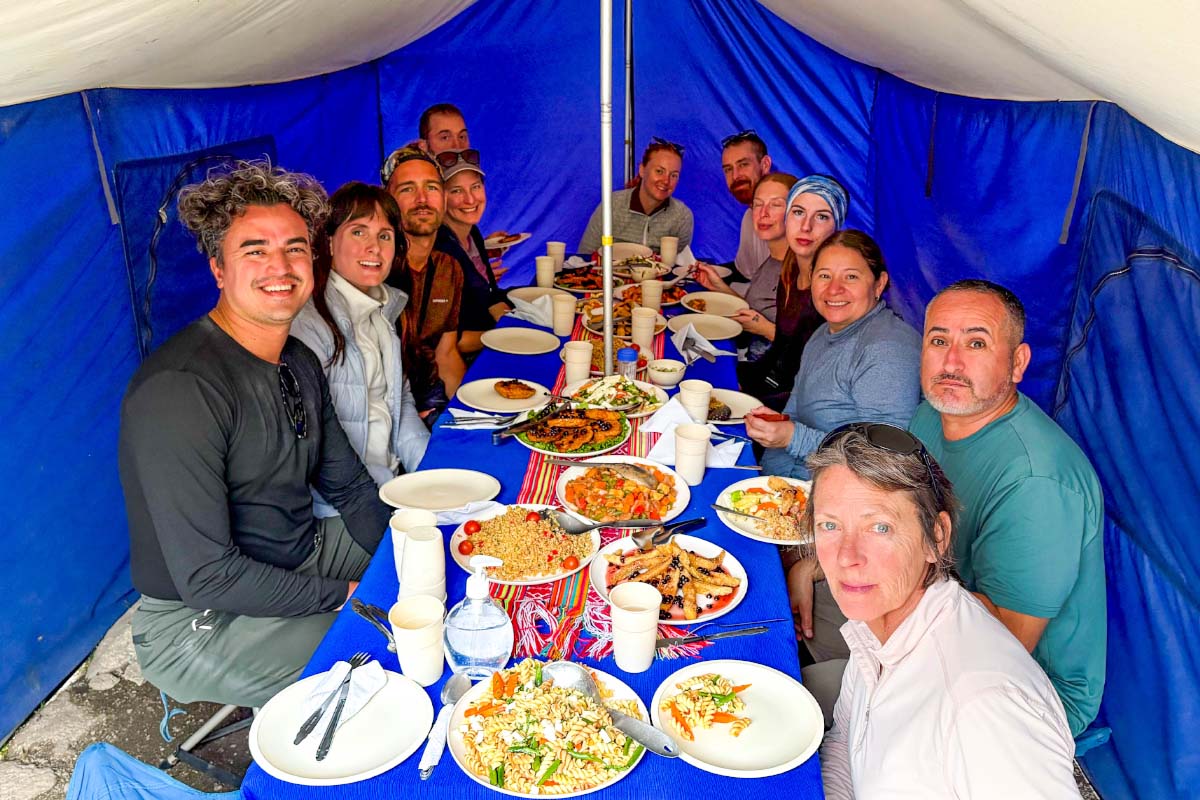Grupo de senderistas sentado alrededor de una mesa con comida servida y bebidas dentro de una carpa azul | TreXperience 