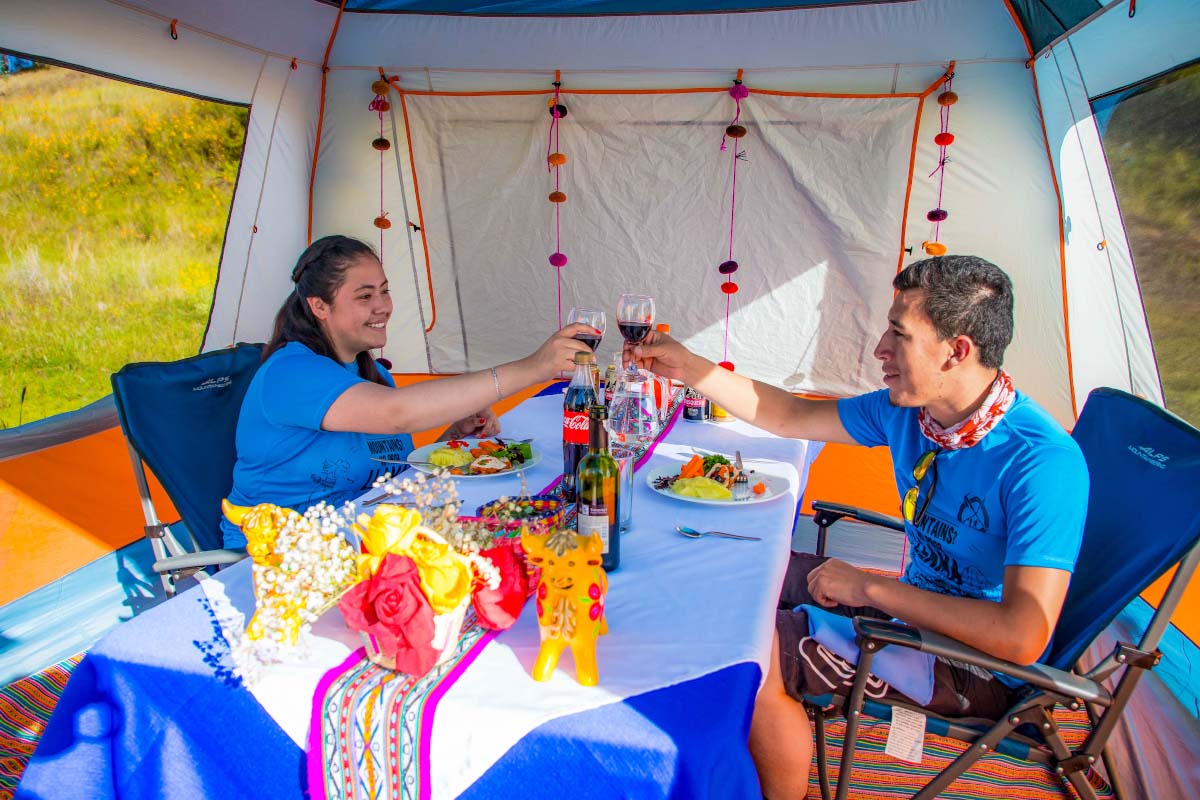 Enjoying gourmet food in the middle of the mountains Tourists enjoying a table with food and drinks inside a colorful tent | TreXperience