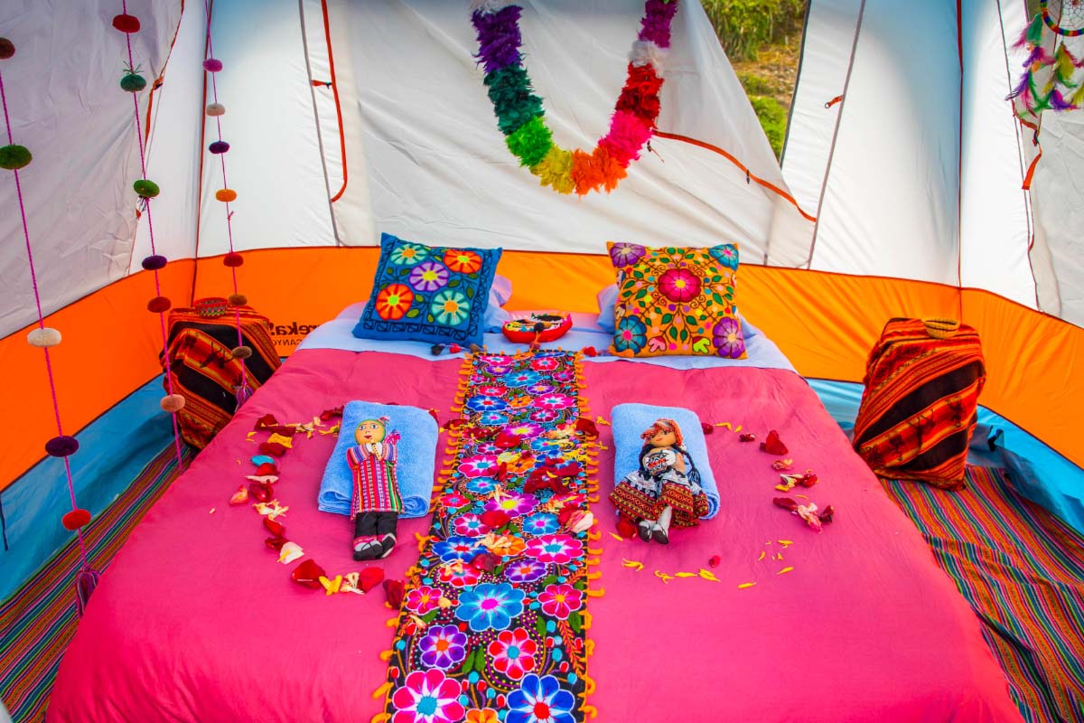 Interior de una tienda de campaña con cama cubierta por textiles coloridos, cojines estampados y adornos colgantes | TreXperience