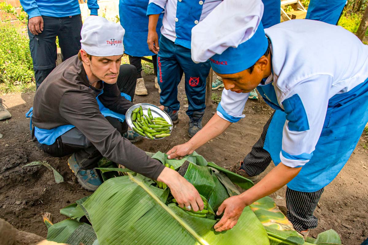 Cocineros junto a turistas con uniforme azul preparando alimentos al aire libre | TreXperience