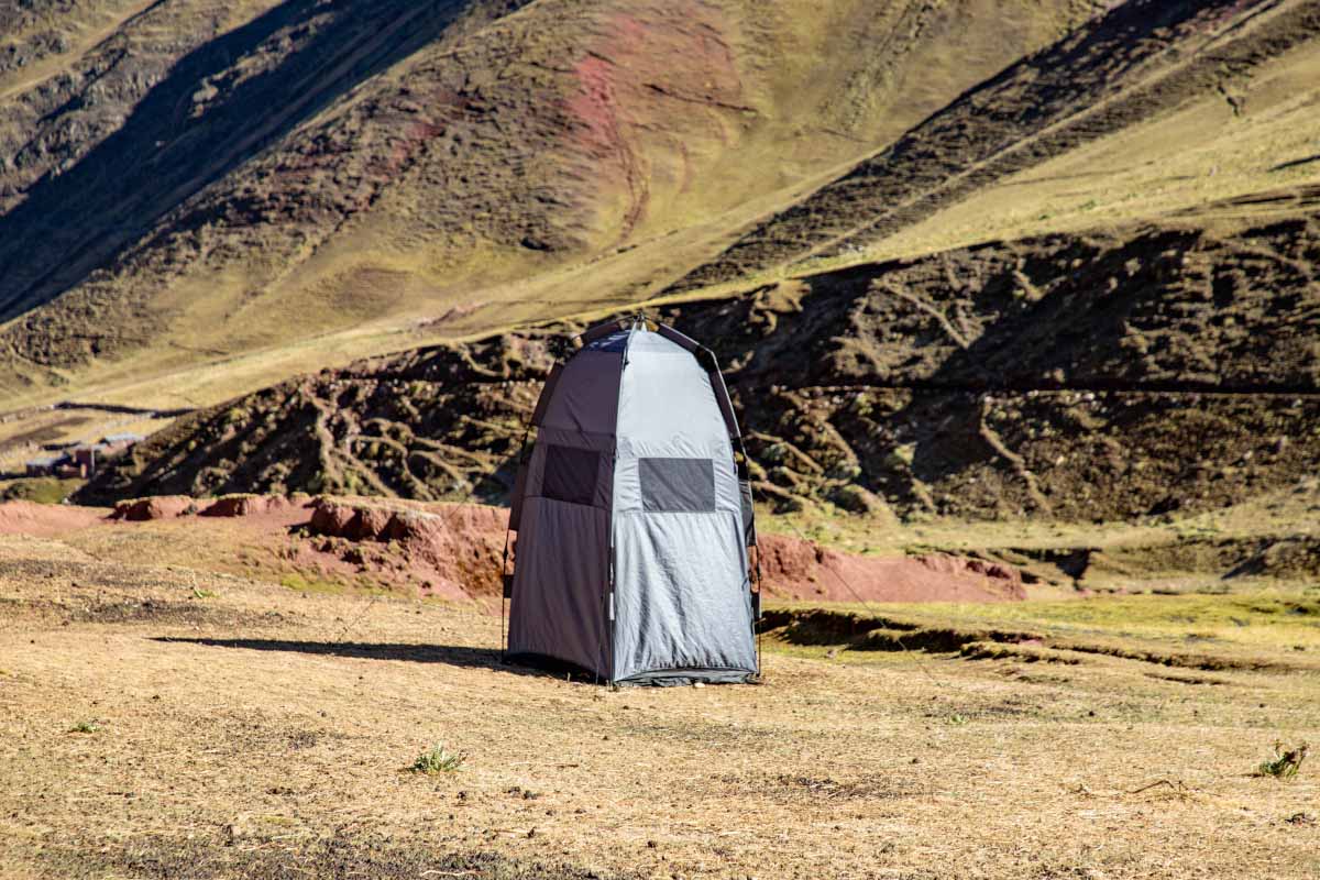Portable toilet installed in the middle of nature Bathroom tent set up on open mountain terrain, surrounded by rocky slopes and low vegetation | TreXperience