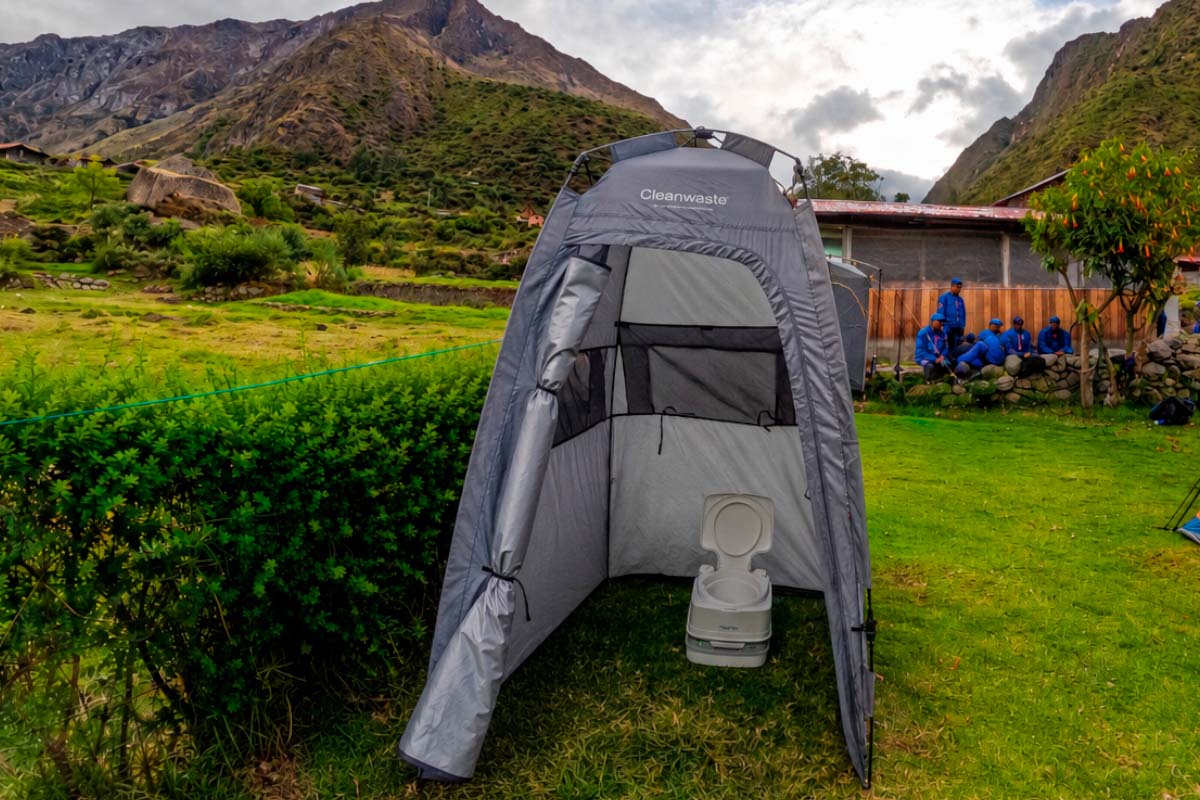 Grey portable toilet cabin in a mountain setting Portable bathroom cabin installed on a green area in a mountain setting | TreXperience