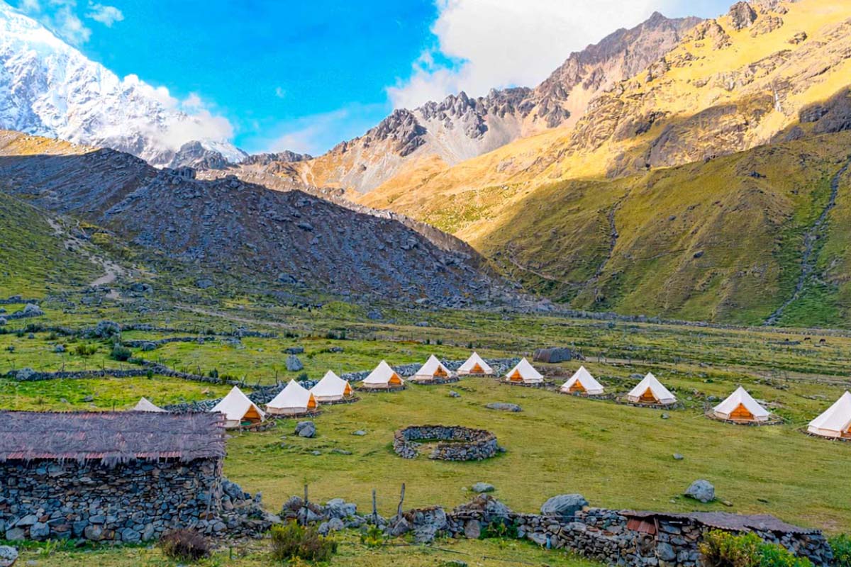 Glamp camp among mountains with snow-capped peaks Camp with several tents on a green area between mountains, with snow-capped peaks in the background | TreXperience