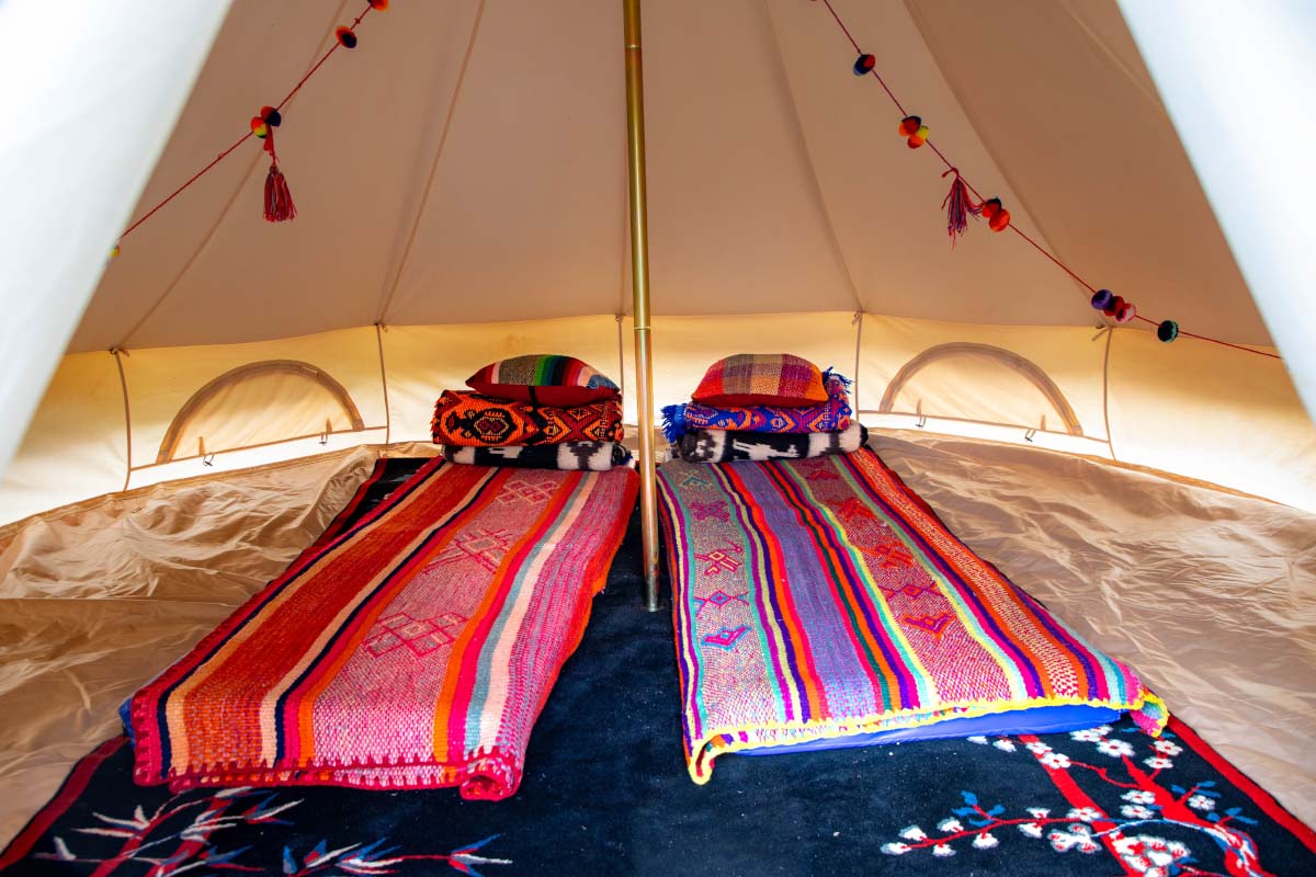 Interior del Salkantay Glamp de TreXperience con dos camas cubiertas por mantas coloridas y almohadas | TreXperience