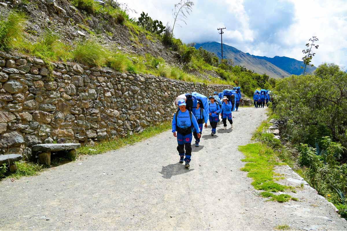 Porters on a path next to a stone wall Group of porters walking along a mountain path next to a stone wall and green vegetation | TreXperience