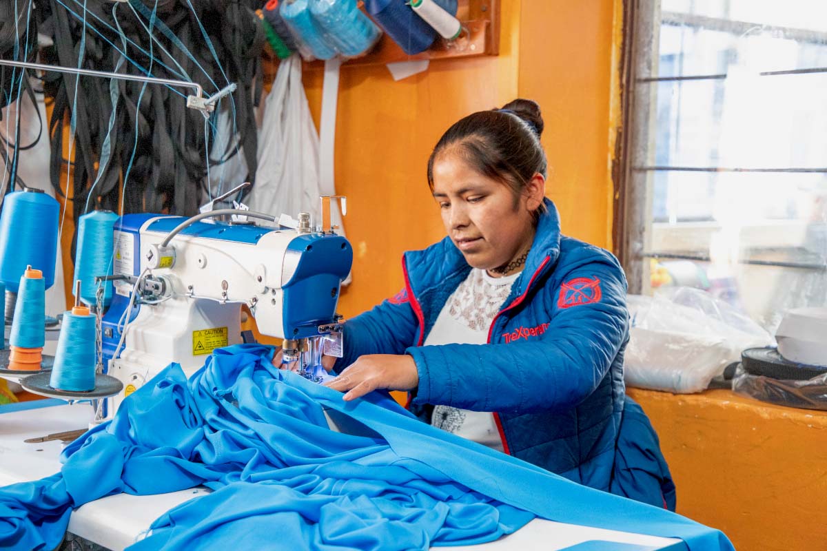 Trabajadora de TreXperience Trabajadora de TreXperience trabajando con tela azul sobre una mesa, con prendas y materiales textiles alrededor | TreXperience