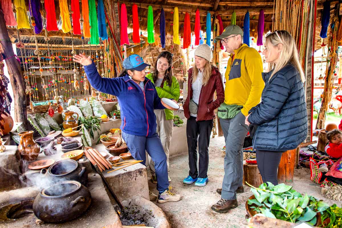 Turistas en experiencias textiles y artesanías de Chinchero Grupo de personas dentro de un puesto con textiles coloridos, prendas colgadas y artesanías exhibidas | TreXperience