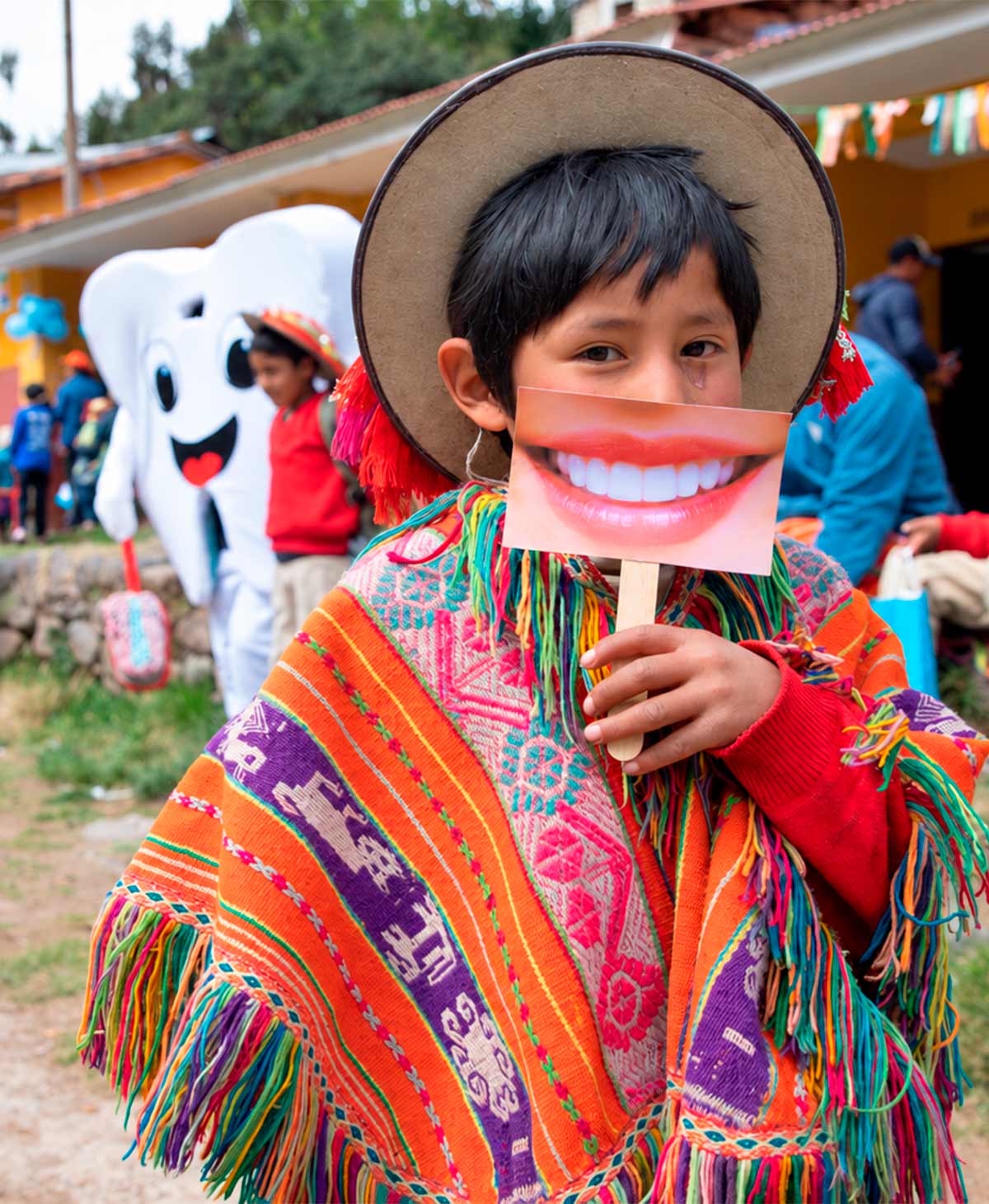 Child in a colorful poncho and hat holding a smile photo prop, with a tooth mascot behind