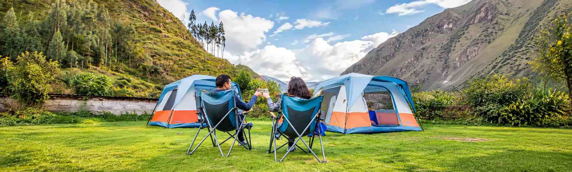 Couple raising their mugs in camp chairs in front of two walk-in tents at an Inca Trail campsite
