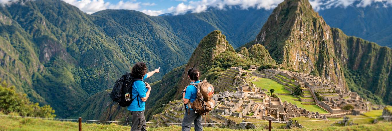 Two hikers with backpacks looking out over Machu Picchu and Huayna Picchu at the end of the Inca Trail