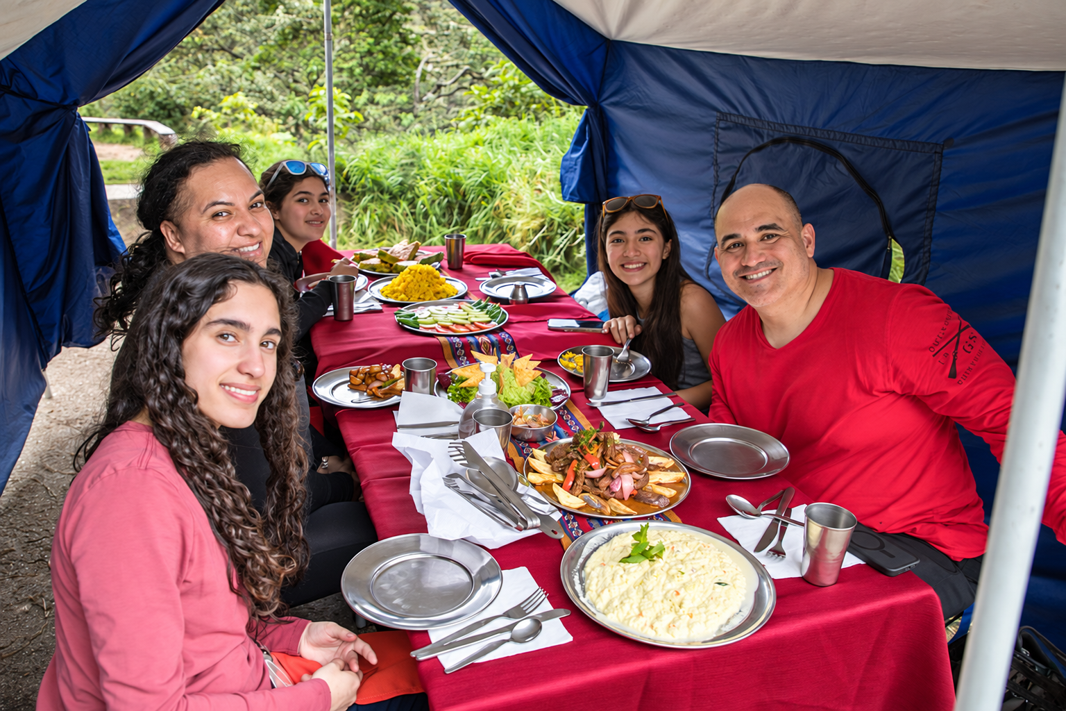 Grupo de viajeros sentado alrededor de una mesa con comida servida y bebidas bajo una carpa colorida | TreXperience