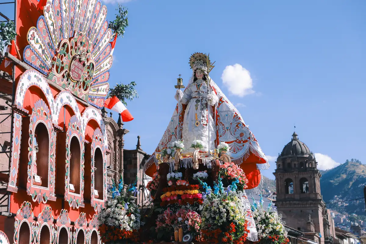 Photo of the Virgin Mary borne in a solemn religious procession, surrounded by reverent participants and ceremonial adornments.