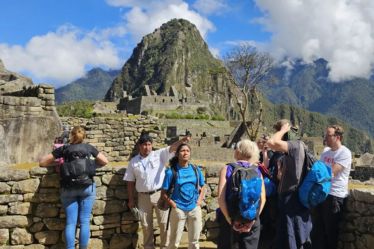 Turistas en la ciudadela de Machu Picchu Machu Picchu Turista de pie en la antigua ciudadela de Machu Picchu, rodeado de construcciones de piedra y paisaje montañoso verde.
