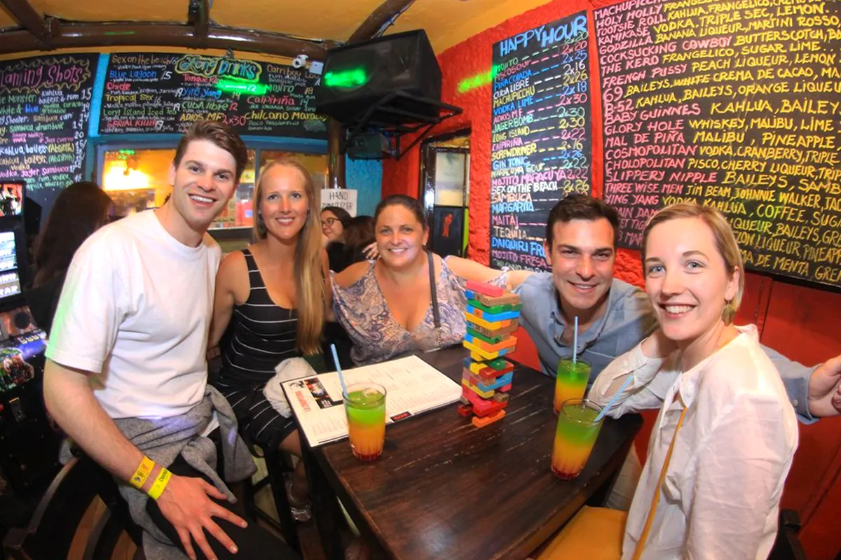 Tourists celebrating with drinks and music at La Chupitería bar.