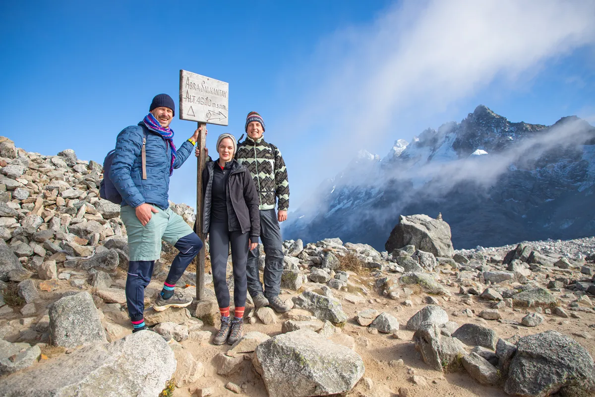 Tourists at Salkantay Pass Group of hikers posing next to the Salkantay Pass sign, with snow-capped mountains and clouds in the background | TreXperience