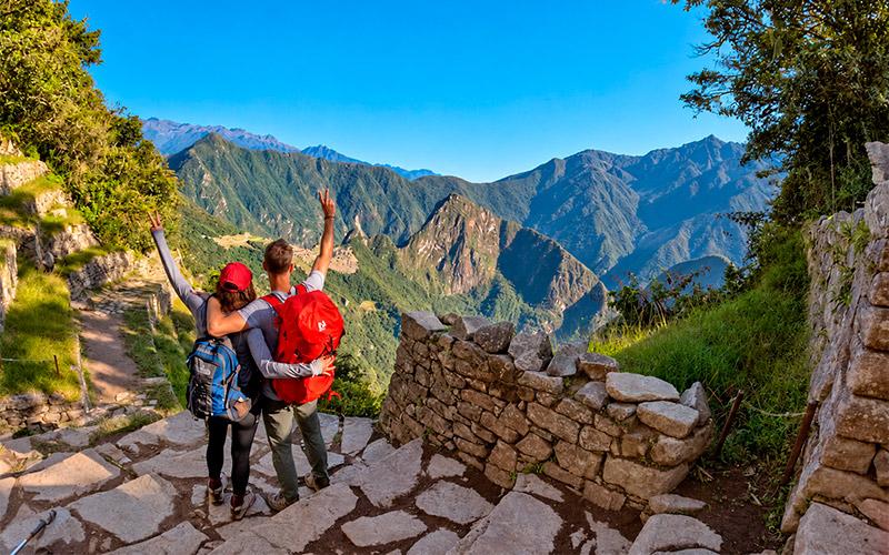 Two hikers with backpacks raising their arms at Intipunku, the Sun Gate, with Machu Picchu in the distance