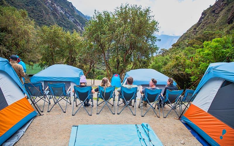 Travelers relaxing in camp chairs beside walk-in tents at a Luxury Inca Trail campsite