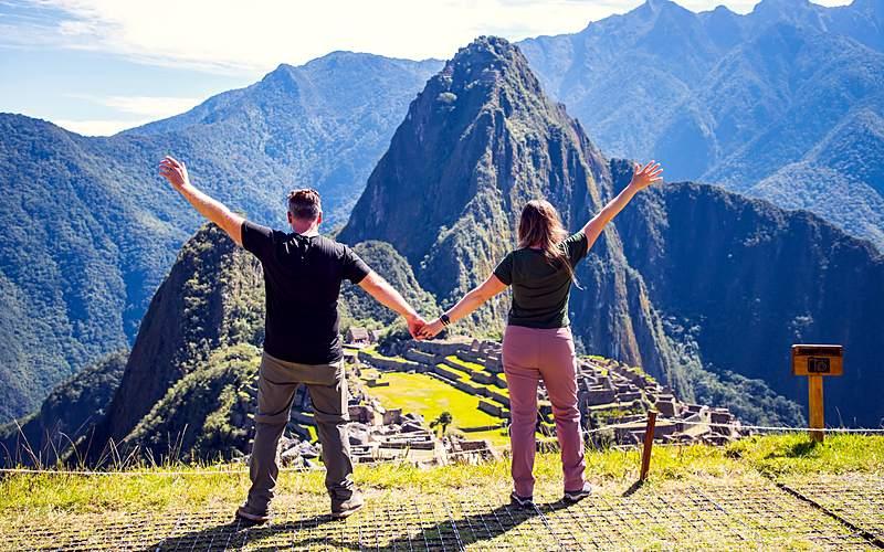Pareja con los brazos abiertos frente a la ciudadela de Machu Picchu en el tour de lujo de 2 días