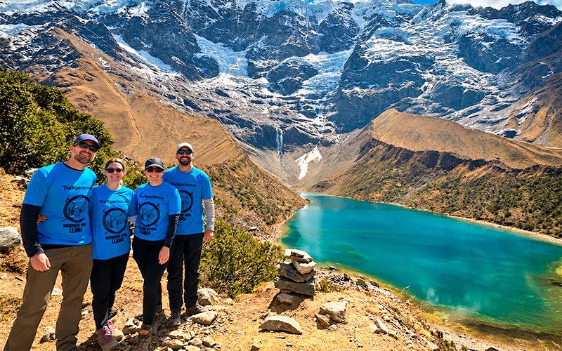 Dos senderistas con bastones posando junto a la laguna Humantay de aguas turquesas y montañas nevadas