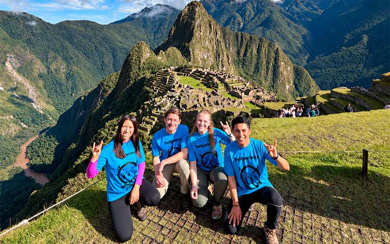 Four travelers in blue shirts posing at Machu Picchu, with Huayna Picchu in the background