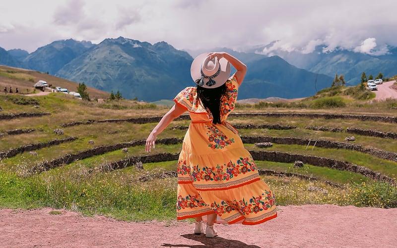 Viajera con vestido amarillo en las terrazas circulares de Moray, Valle Sagrado, en el tour de lujo de 4 días