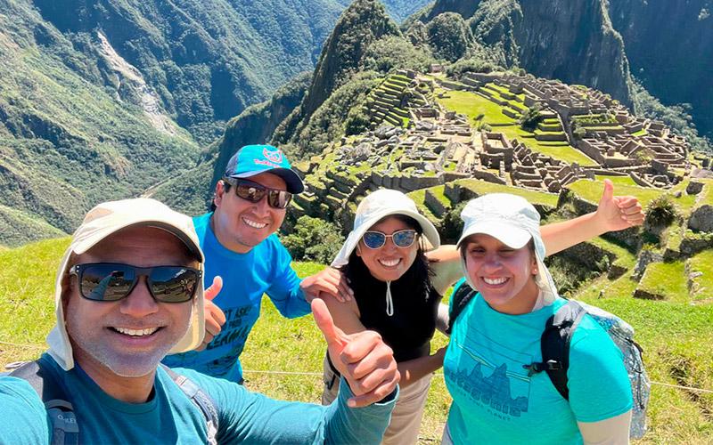 Tres viajeros y un guía de TreXperience tomándose una selfi con Machu Picchu y Huayna Picchu al fondo