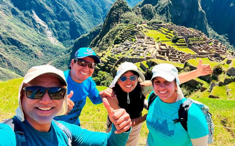 Three travelers and a TreXperience guide taking a selfie above Machu Picchu, with Huayna Picchu behind