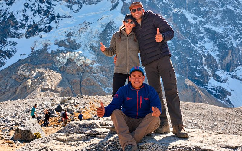 Three hikers giving thumbs up on a rocky viewpoint in front of snowy Salkantay