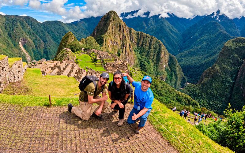 Two travelers and a TreXperience guide posing at Machu Picchu, with Huayna Picchu in the background