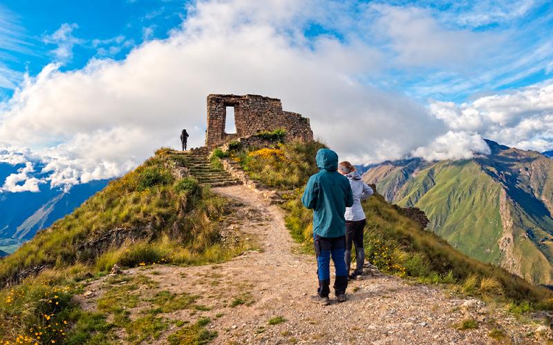 Senderistas en el camino a Intipunku, la Puerta del Sol de Ollantaytambo, con montañas y nubes al fondo