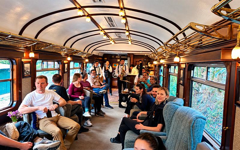 Pasajeros en sillones azules del tren Vistadome Observatory con músicos tocando al fondo