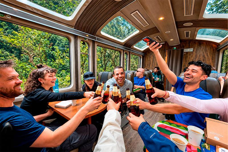 Viajeros brindando con botellas de cerveza en un tren panorámico, con un bosque tras las ventanas