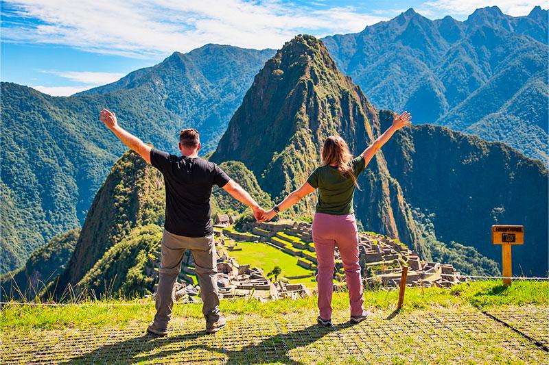 Pareja de espaldas tomada de la mano en un mirador de Machu Picchu con Huayna Picchu al fondo