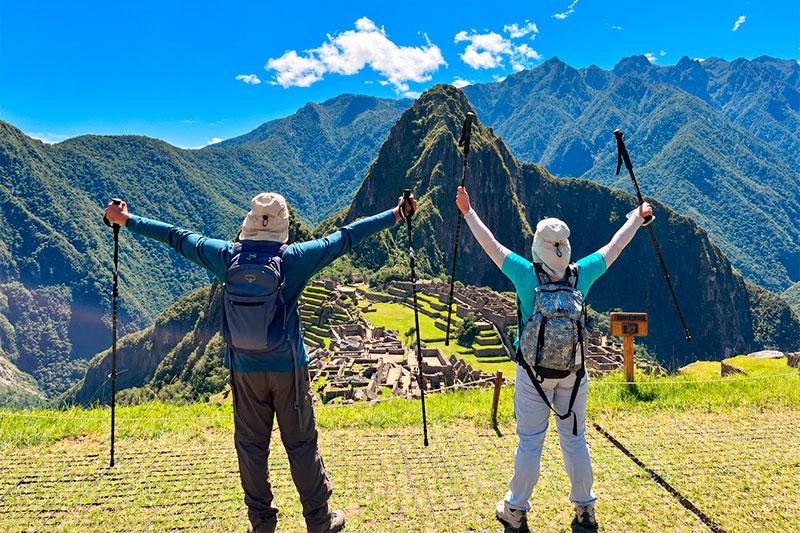 Pareja levantando sus bastones de trekking frente a machu picchu