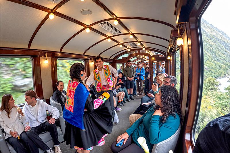 Dos bailarines con trajes bordados de colores actuando ante los pasajeros dentro de un vagón de tren