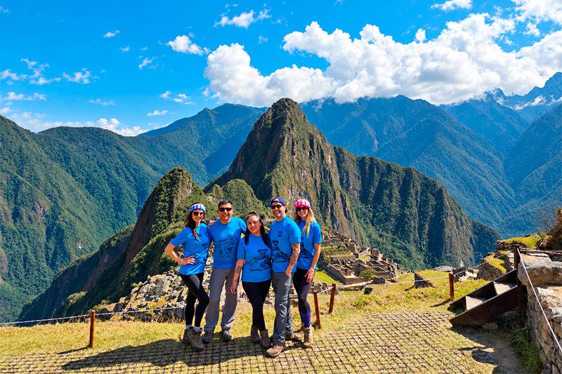 Cinco viajeros con camisetas azules de TreXperience posando en Machu Picchu, con Huayna Picchu al fondo