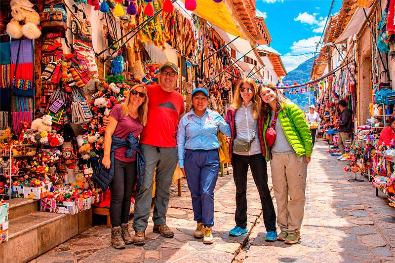Four travelers and a TreXperience guide among market stalls displaying colorful textiles and Andean crafts