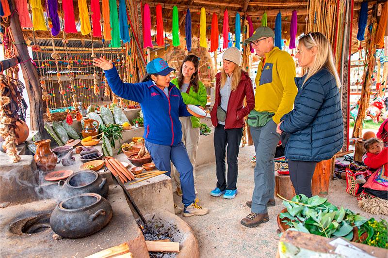 Guía explicando el teñido de lana a cuatro viajeros entre ollas humeantes y madejas de colores en un taller textil
