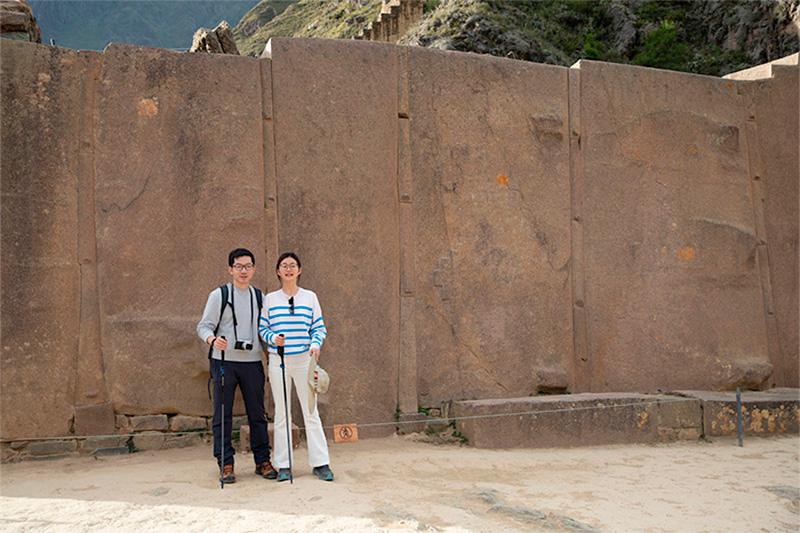 Dos viajeros con bastones frente al Muro de los Seis Monolitos del Templo del Sol de Ollantaytambo
