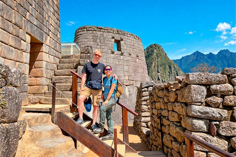 Dos viajeros posando en una escalera de madera junto al Templo del Sol de Machu Picchu