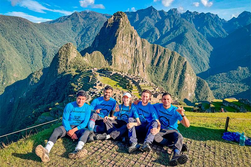 Cinco viajeros con camisetas azules de TreXperience sentados con Machu Picchu y Huayna Picchu al fondo