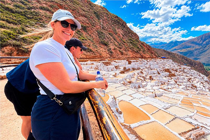 Two travelers beside a wooden railing overlooking the salt ponds of Maras in the Sacred Valley