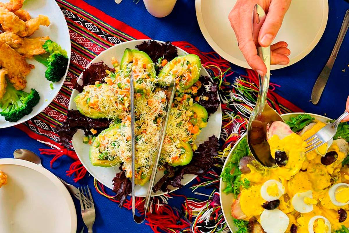 Almuerzo servido sobre un mantel colorido con platos variados y una persona sirviendo comida peruana en un plato | TreXperience