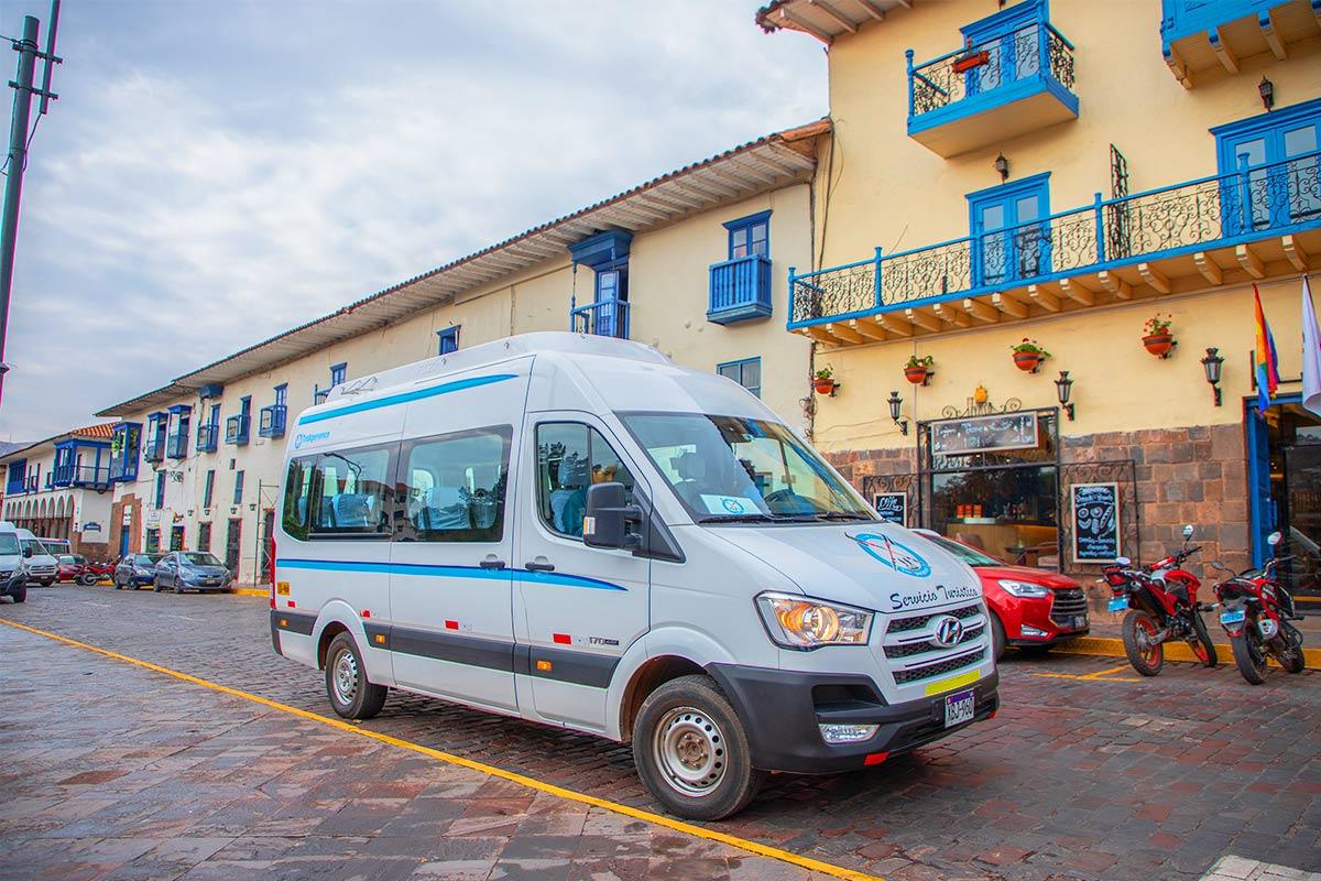 Van blanca estacionada en una calle empedrada junto a edificios con balcones azules | TreXperience