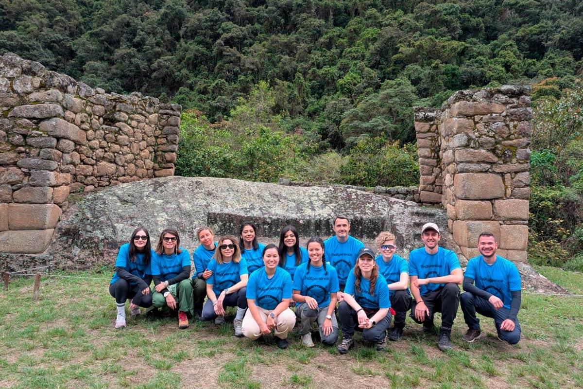 Grupo de viajeros con camisetas azules posando junto a ruinas de Chachabamba rodeadas de vegetación | TreXperience